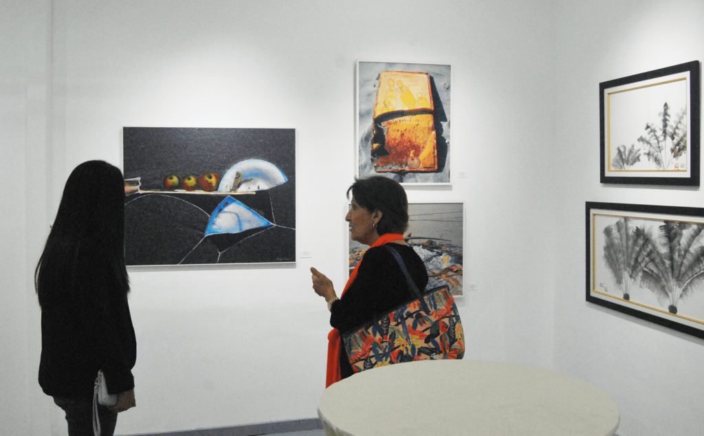Margarita Álvarez de Martínez conversa junto a una asistente de la exposición "Convergencias y Divergencias" en Izalco.art.